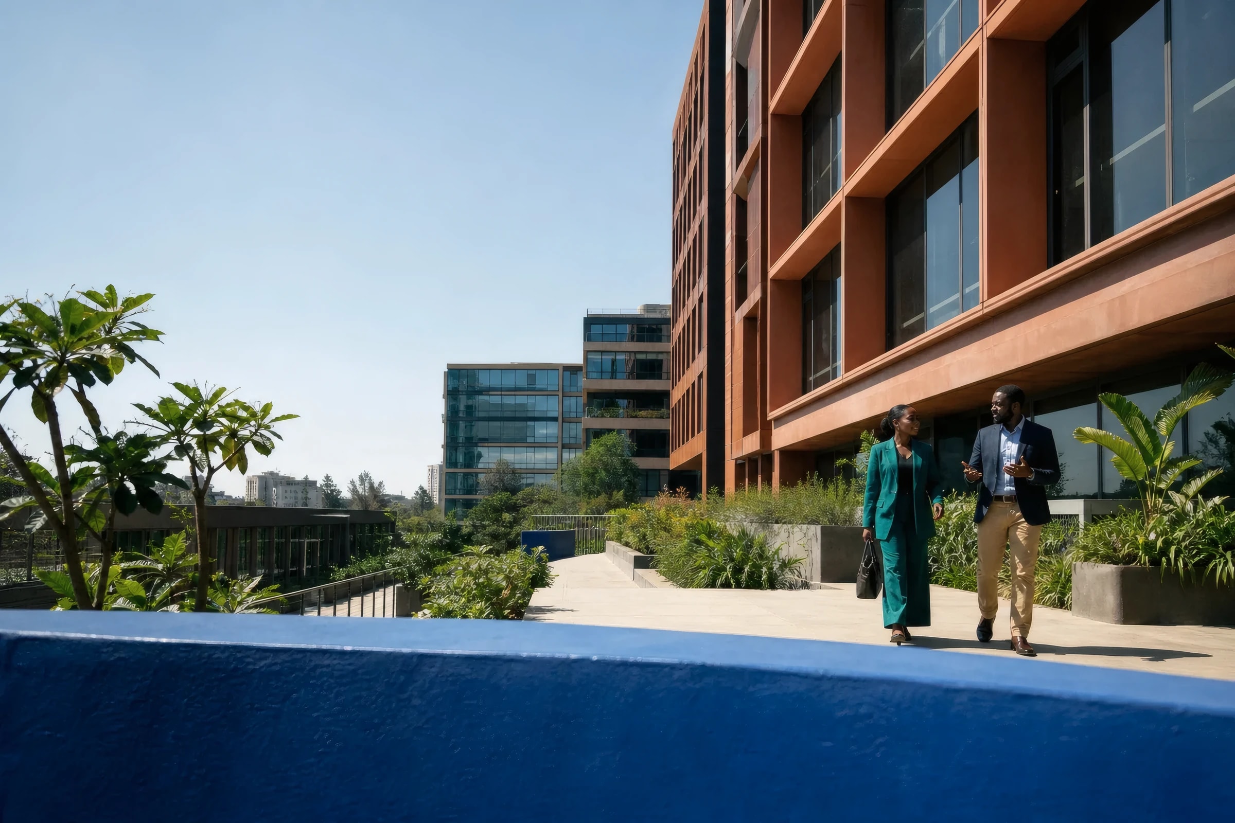 Two professionals in conversation walking along a landscaped terrace between modern Nairobi office buildings